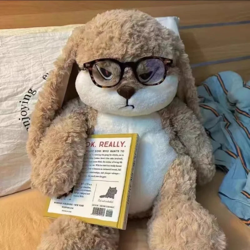 Conejo de peluche con gafas y un libro en la cama
